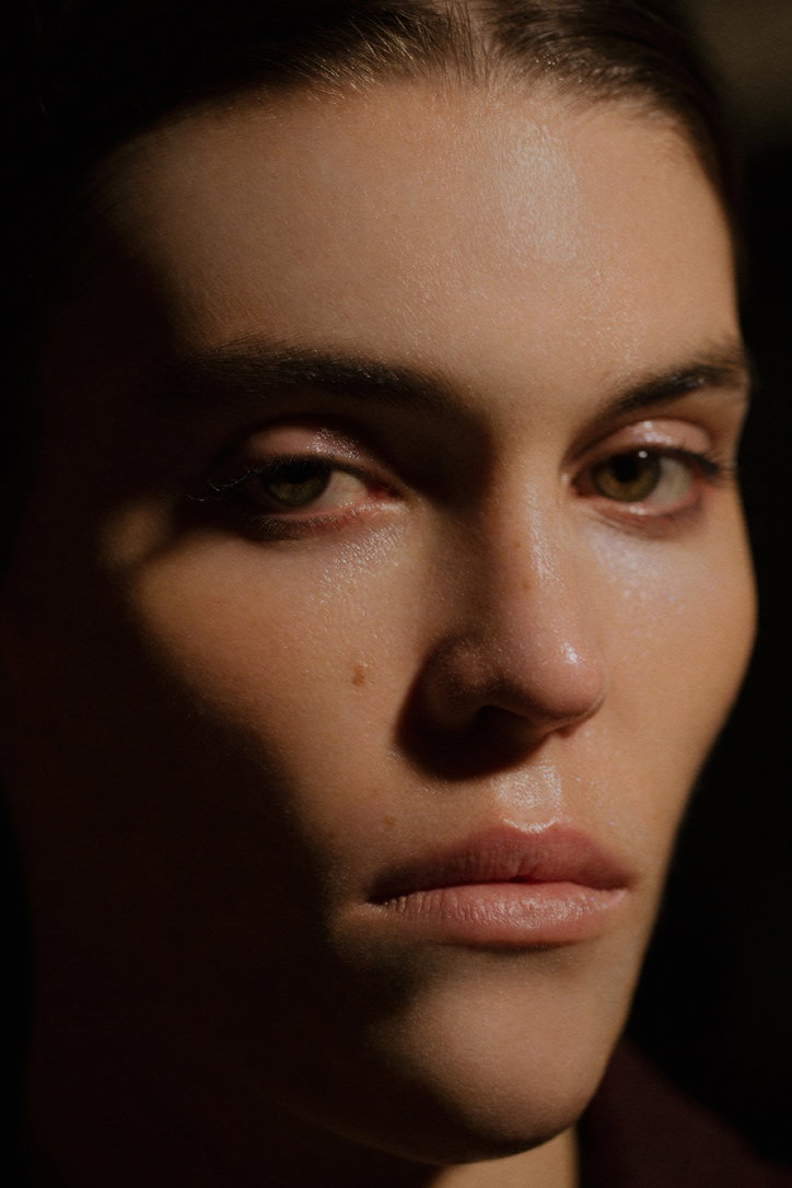 A close-up portrait of a person looking directly at the camera. Half of their face is cast in deep shadow, while the other half is brightly lit.