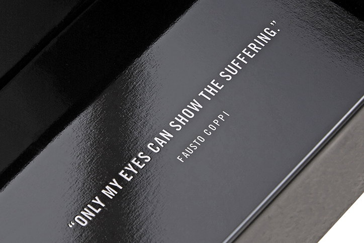 A close-up of a glossy black surface featuring a white quote that reads “Only my eyes can show the suffering.” The name “Fausto Coppi” is printed in smaller text below.