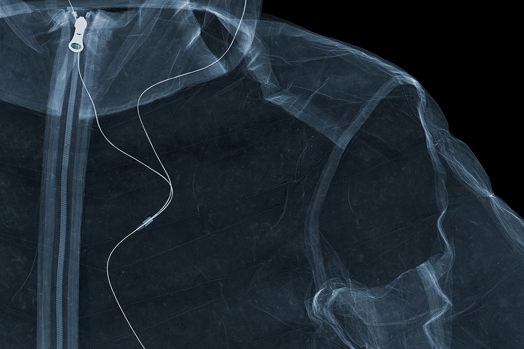 An x-ray of a person wearing a zipped jacket. A thin wire runs from the collar down across the chest.