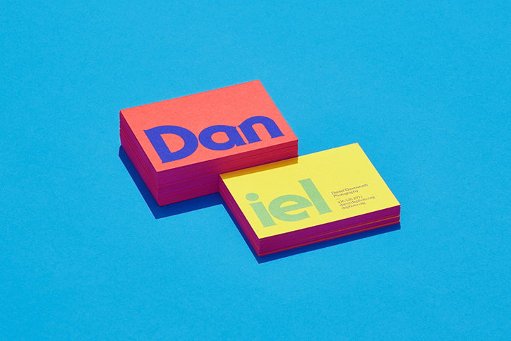 Two stacks of business cards sit on a bright blue background. The top card of the first red stack reads “Dan” in blue, while the top card of the second yellow stack reads “iel” in white.