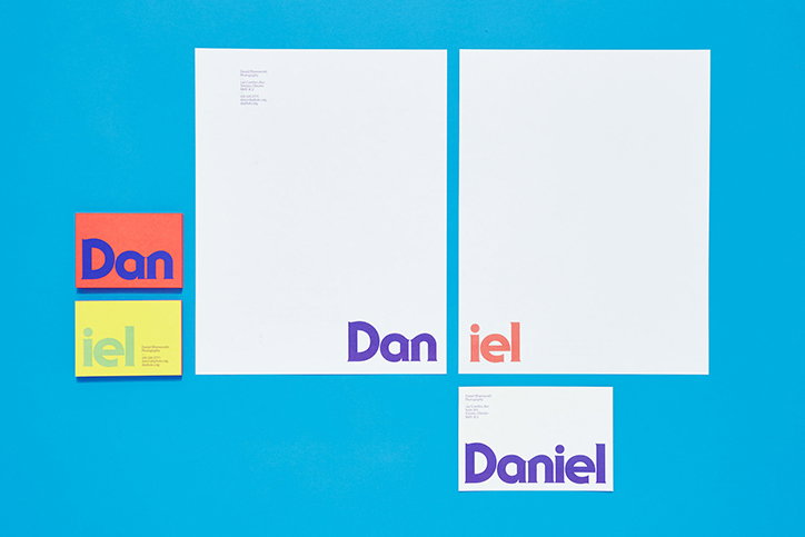 A collection of stationery items laid out on a bright blue background. The branding features the name “Daniel” split across different pieces of paper in purple and orange.