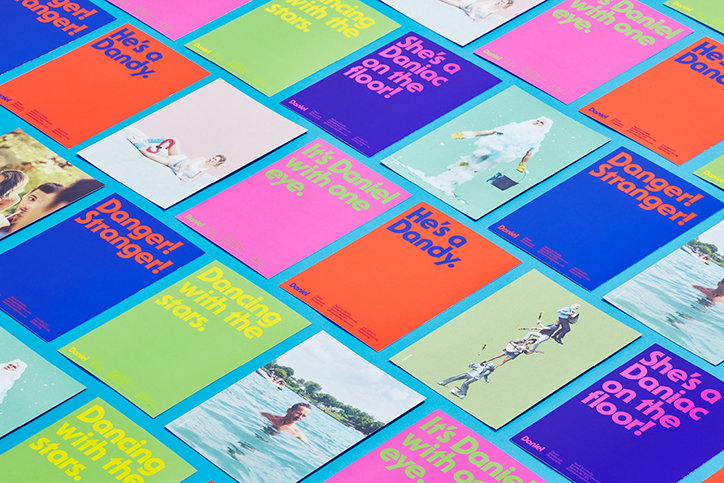 A grid of colourful posters in blue, red, pink and green laid across a bright blue surface. The posters feature photographs of people and bold text including “Danger! Stranger!”, “He’s a Dandy.” and “Dancing with the stars.”