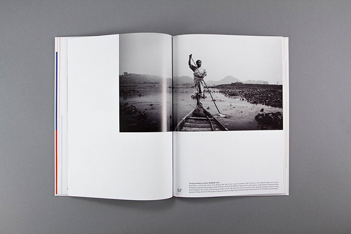 An open book displays a black and white photograph of a person standing in a shallow body of water. They hold a long pole and stand beside a small wooden boat.