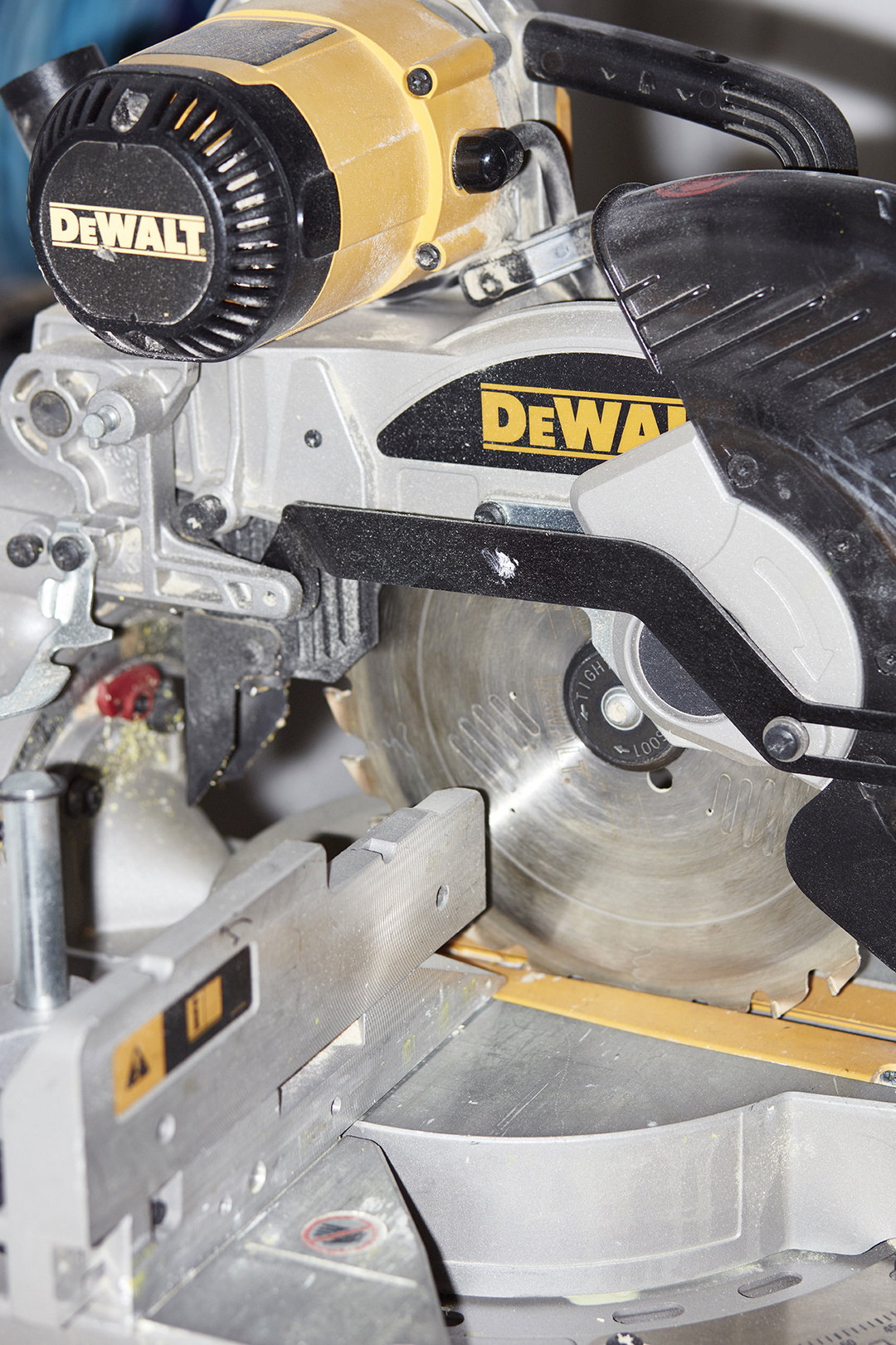 A close-up of a yellow and grey Dewalt mitre saw. The circular blade is positioned over a metal base, with dust settled across the machine’s surfaces.