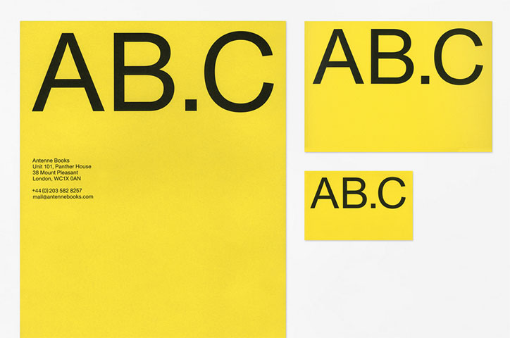 Three yellow printed cards of different sizes, each featuring the bold black text “AB.C”. The largest card includes the address and contact details for Antenne Books in London.