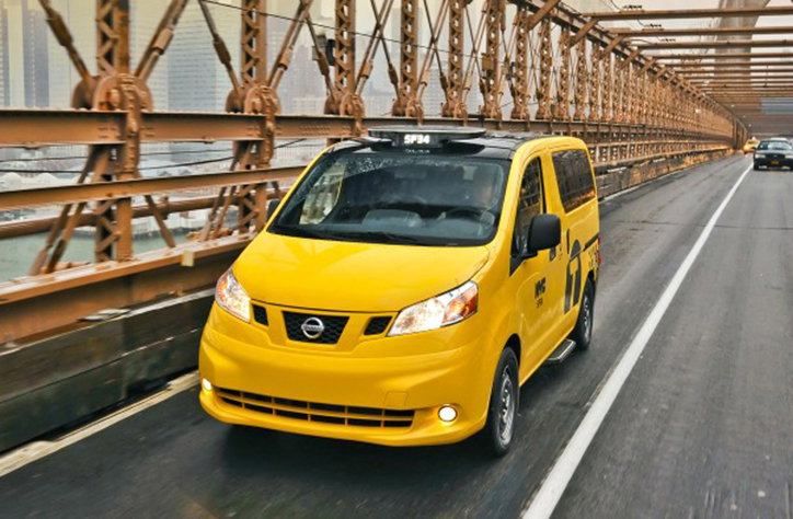 A yellow Nissan taxi drives across a bridge with a brown steel lattice structure. The vehicle is captured from a front-angle view as it moves along the road.