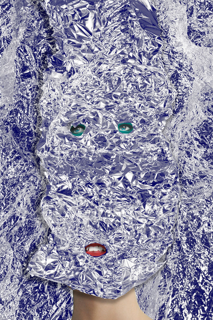 A person’s head and face are completely covered in crumpled aluminium foil. Only their eyes and mouth are visible through small gaps in the foil.