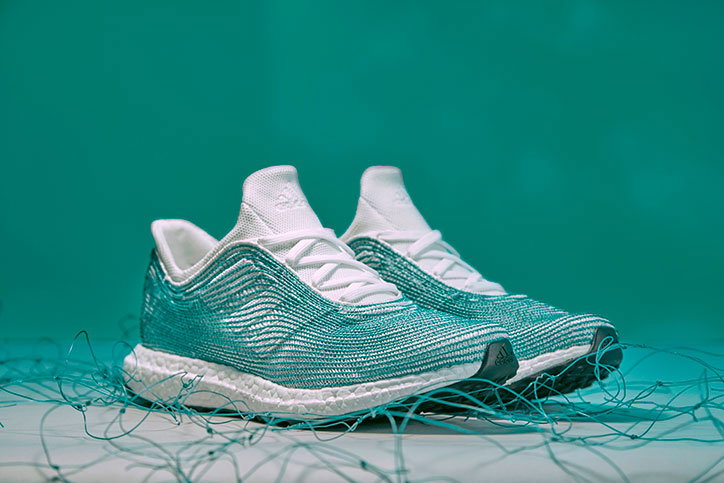 A pair of teal and white Adidas trainers sit on a white surface. They are surrounded by a tangle of thin, teal-coloured wires against a matching teal backdrop.