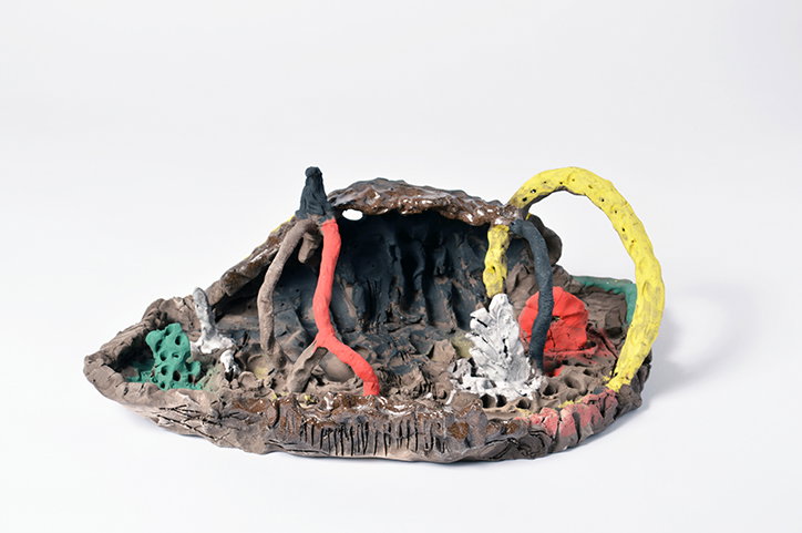 A ceramic sculpture of a rugged, brown landscape with a hollowed-out centre. Bright red, yellow and green organic forms wind through the textured terrain.