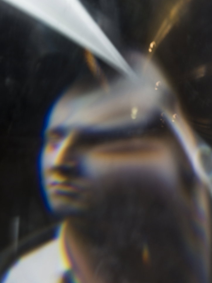 A blurred, distorted portrait of a person. A bright beam of white light cuts across the top of the frame, creating a smeared, prismatic effect.