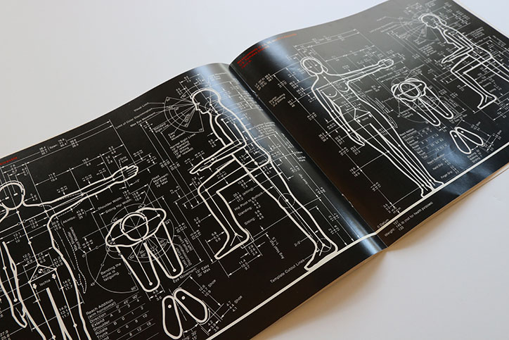 An open book with black pages featuring white technical diagrams of human figures. The pages are filled with precise measurements, lines and labels detailing body proportions and movement.