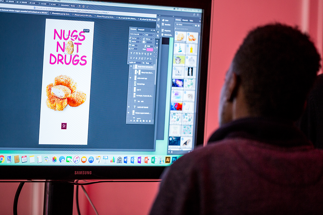 A person looks at a computer screen showing a graphic design in progress. The artwork features a pile of chicken nuggets under the bold text “NUGS NOT DRUGS”.