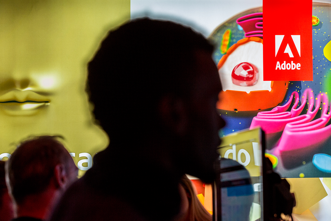 A silhouette of a person in the foreground looks towards a bright screen. The screen displays a colourful 3D render and the Adobe logo.