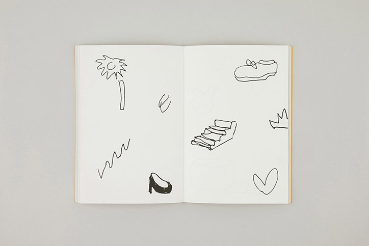 An open sketchbook featuring a series of simple black ink doodles on white pages. The drawings include a flower, a shoe, a set of stairs, a heart and a crown.