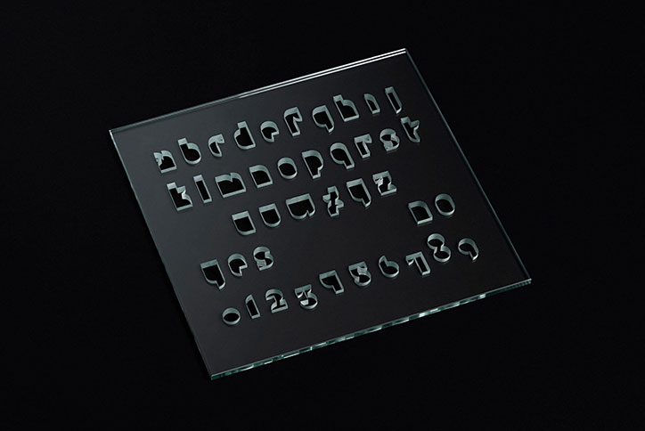 A clear glass pane with a series of letters and numbers cut out of the surface. The characters are arranged in five neat rows against a black background.