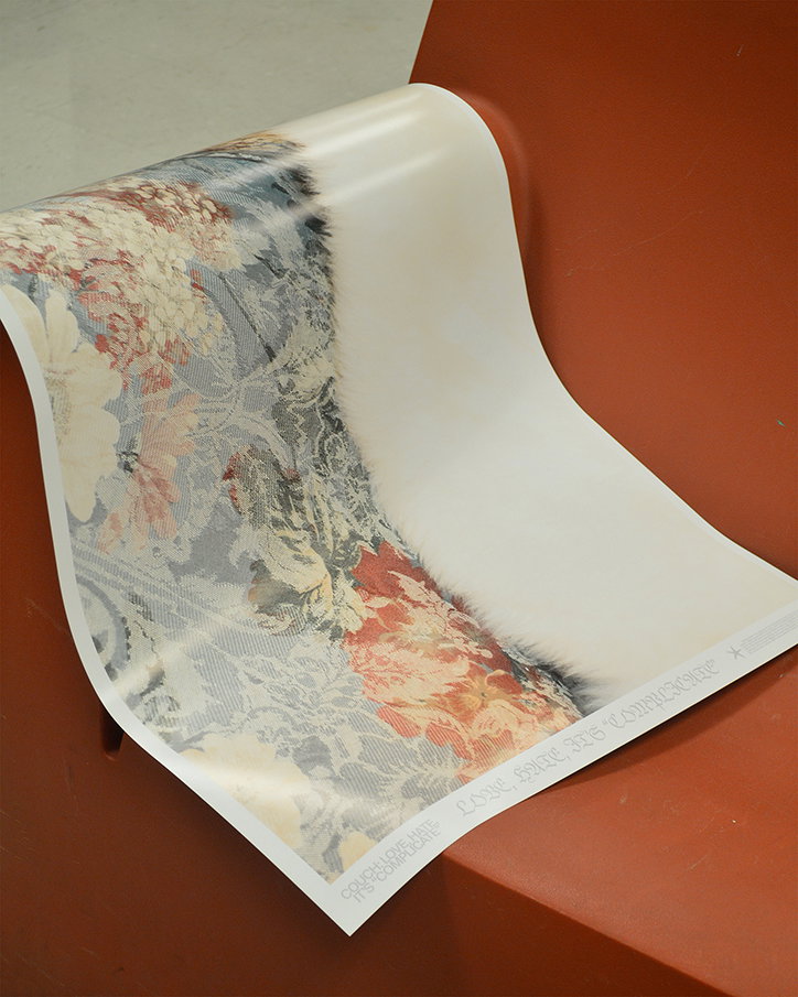 A printed poster drapes over a terracotta-coloured surface. The image features a soft-focus floral pattern in muted reds and blues, alongside a white, furry texture. Small text along the bottom edge reads “LOVE HAVE ITS COMPLICATIONS”.