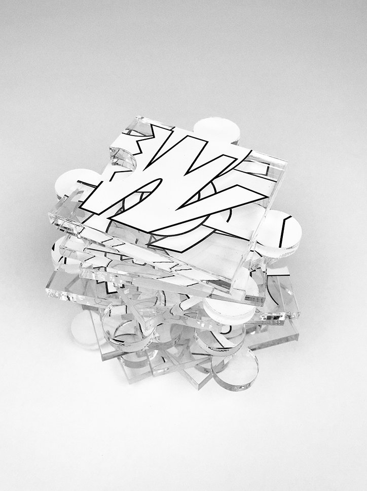 A sculpture made of stacked, transparent acrylic sheets. Bold, black-and-white graphic shapes are printed across the layers, creating a fragmented 3D effect.