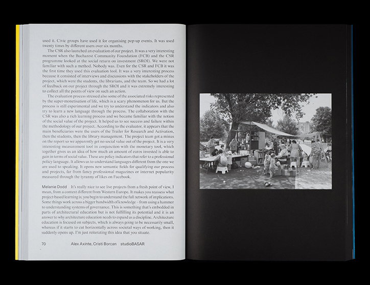 An open book showing a page of dense text opposite a black-and-white photograph. The image depicts a group of people gathered around a table in a sparsely furnished room.