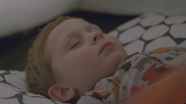 A child sleeps soundly on a patterned pillow. They wear a colourful T-shirt with a playful print.