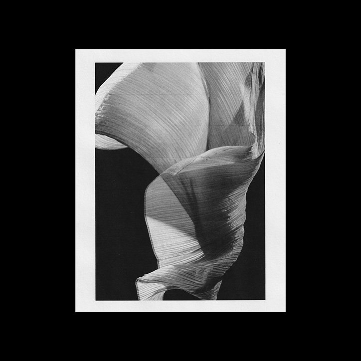 A black and white photograph of a piece of sheer, textured fabric twisting and billowing against a dark background. The light catches the fine ridges of the material, creating a sculptural, fluid shape.