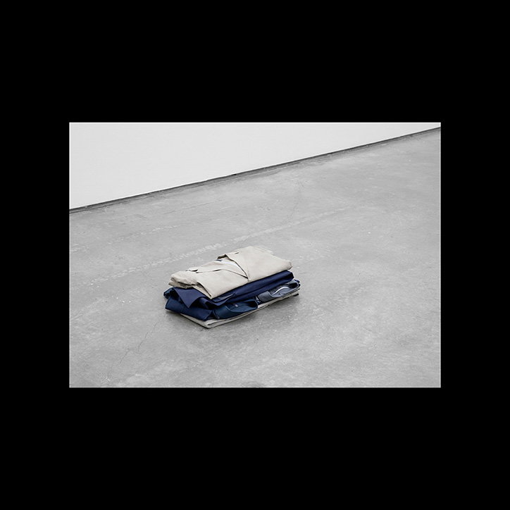 A neat stack of folded clothes sits on a grey concrete floor. The pile consists of a beige garment on top of a dark blue one.