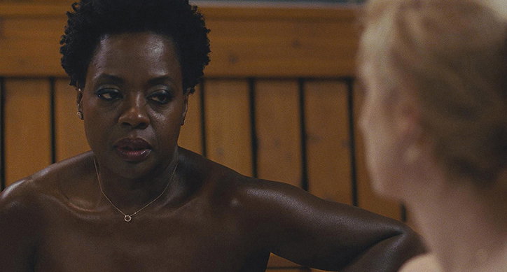 Viola Davis looks towards another person with a serious expression. They are both in a wooden sauna, with the light catching the moisture on their skin.