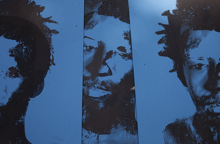 Three high-contrast portraits of a person are printed on blue paper. The images are rendered in a grainy, ink-like style with deep black shadows.