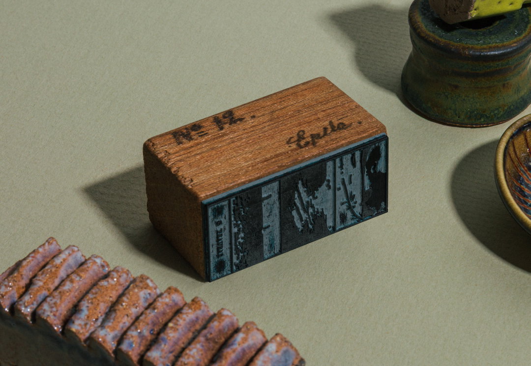 A rectangular wooden block with a carved relief on its side. Handwritten ink on the top surface reads “No 12.” and “Epila.”.