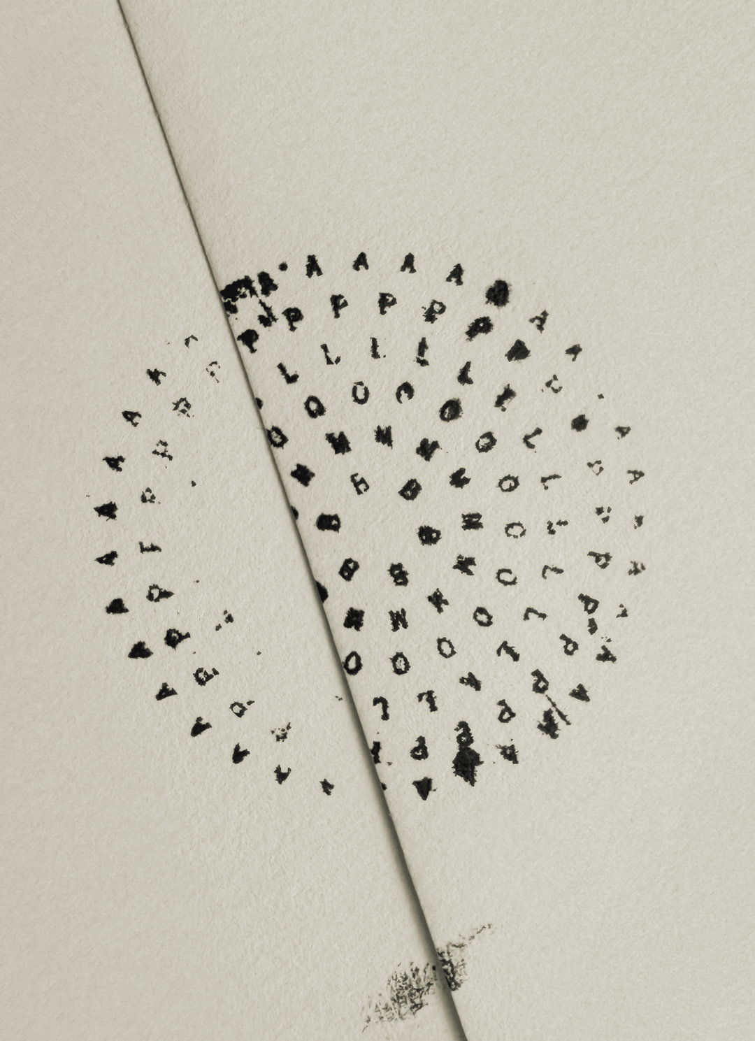 A circular arrangement of black stamped letters on off-white paper. A diagonal crease runs through the centre of the circle, splitting the letters.