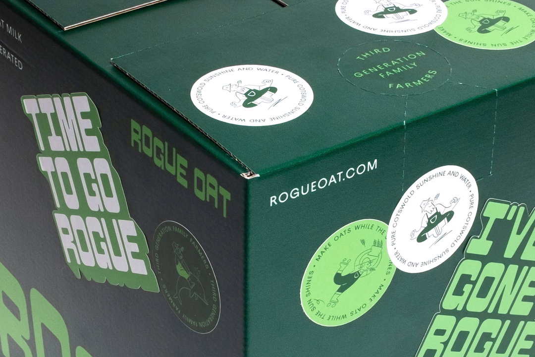 A close-up of a dark green cardboard box for Rogue Oat. Bold, light green text reads “TIME TO GO ROGUE” and “I’VE GONE ROGUE”, alongside the brand name and website.