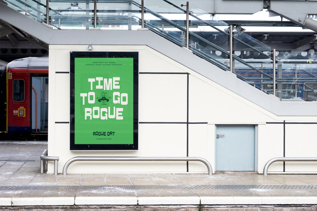 A green advertising poster on a white station wall reads “TIME TO GO ROGUE”. Smaller text at the bottom identifies the brand as “ROGUE OAT”.