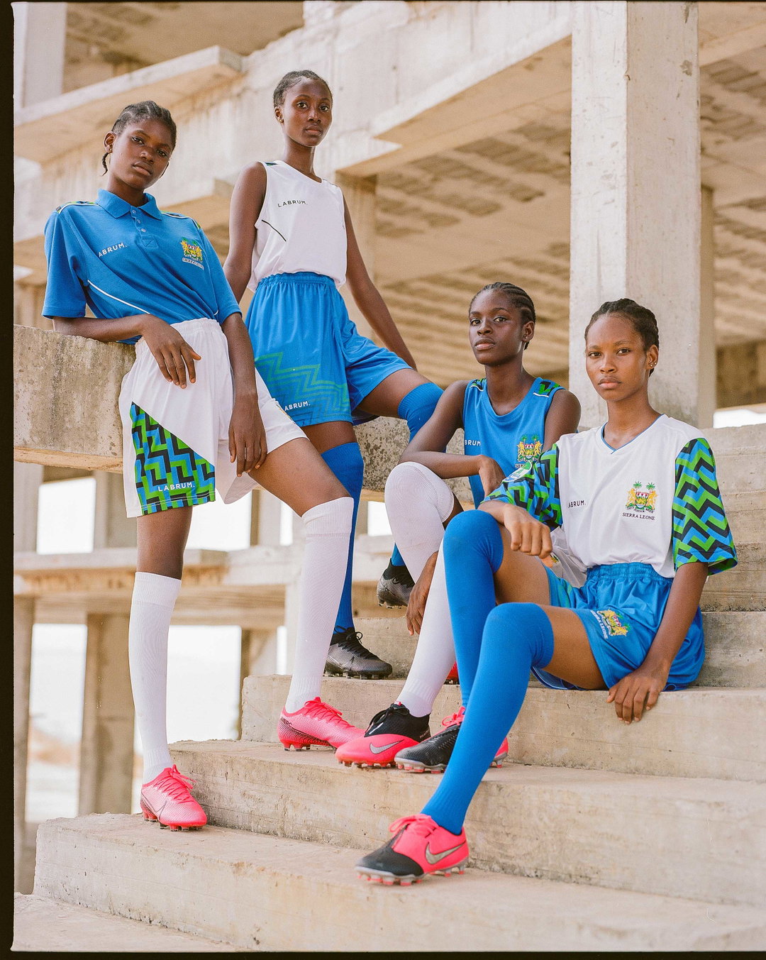 Four people pose in a concrete building shell, wearing blue and white sportswear. The clothing features green and yellow geometric patterns and the word “Labrum”.