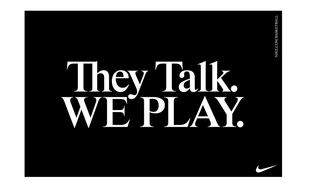 A black poster with bold white text that reads “They Talk. WE PLAY.” The Nike swoosh logo appears in the bottom right corner.