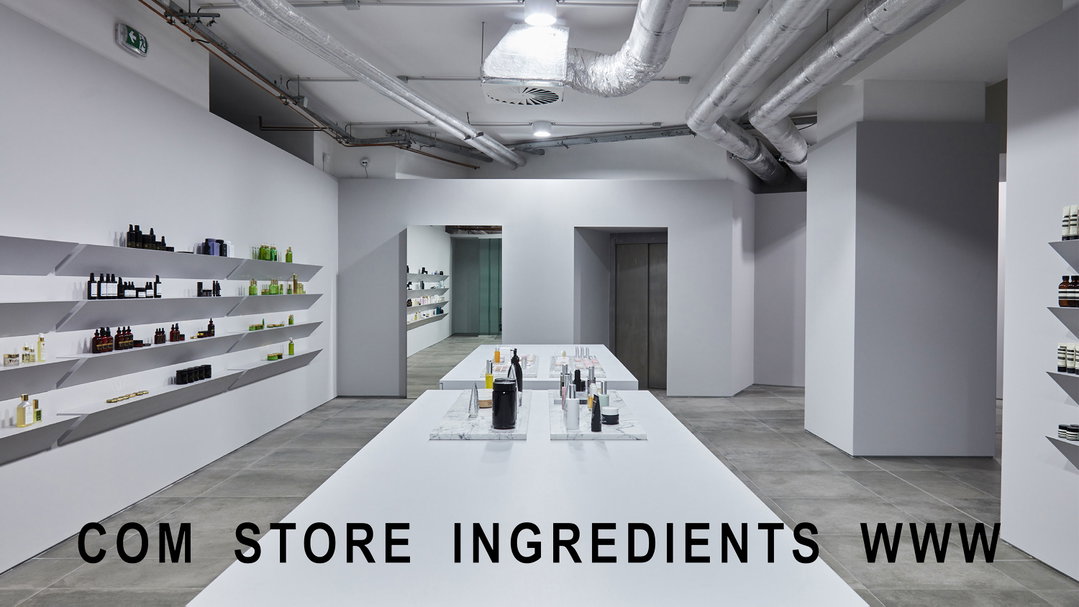 A minimalist white retail space with industrial exposed piping along the ceiling. Products are displayed on long white tables and thin wall shelves, with the text “COM STORE INGREDIENTS WWW” laid over the foreground.